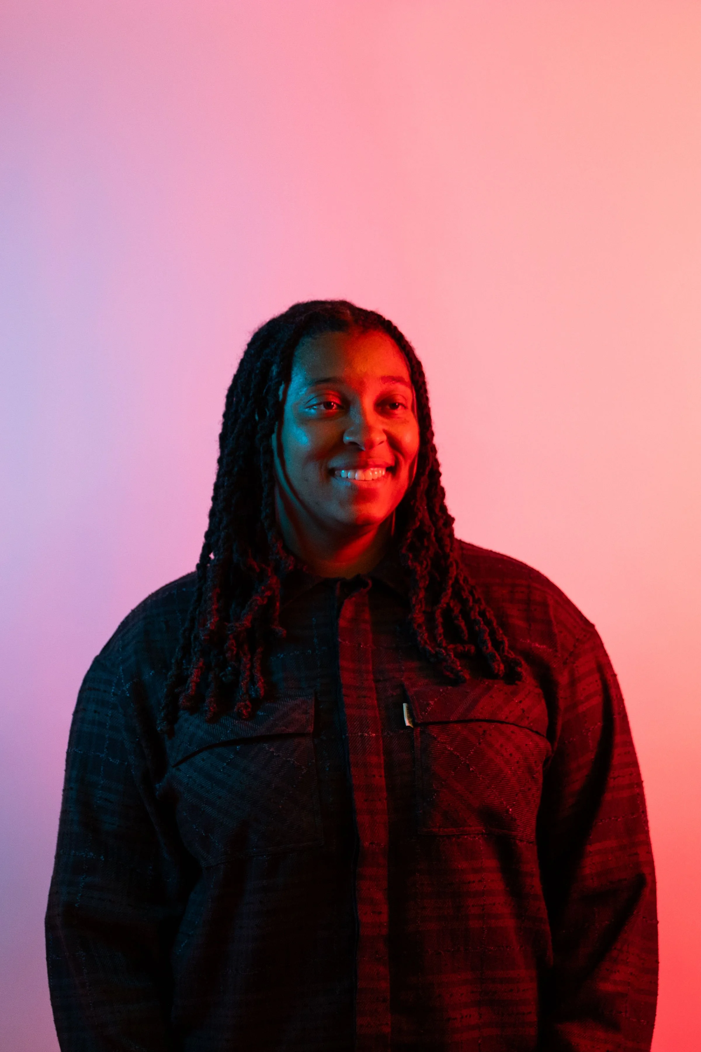 Portrait of a smiling woman with dreadlocks against a pink and blue color gradient background.