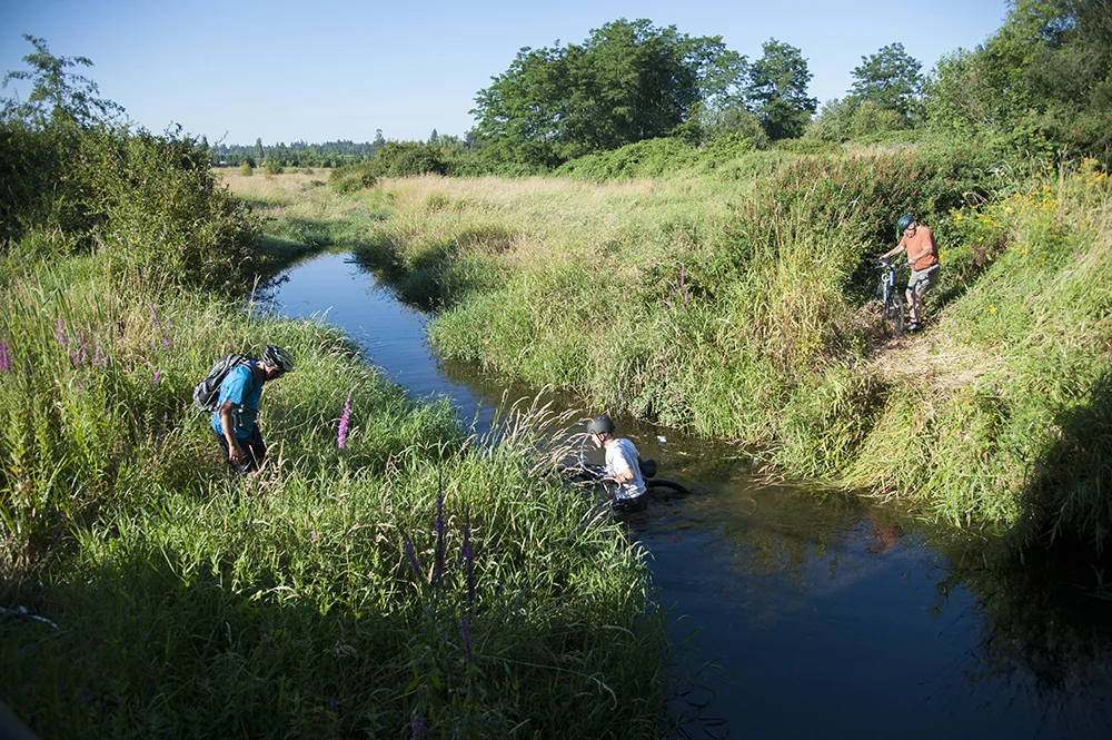 Tris White carrying his bicycle through the river