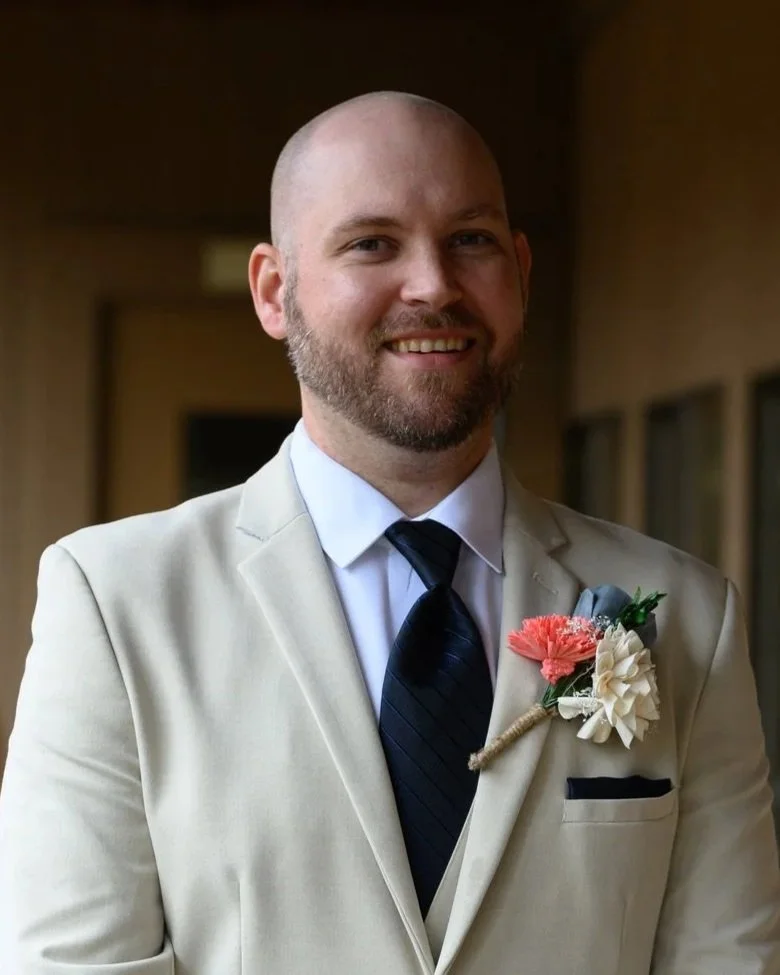 man in a beige suit smiling with faded background