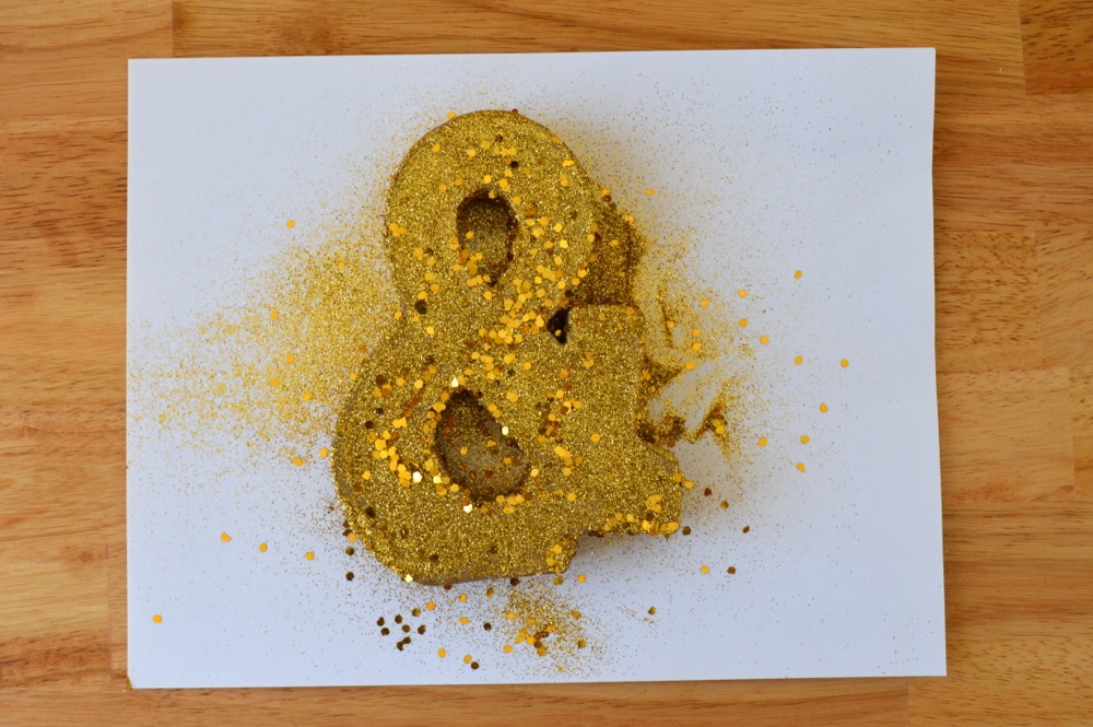 Paint each side of the cardboard ampersand with glue then shake on glitter, repeating for each side (except the bottom where it will rest on the cake).