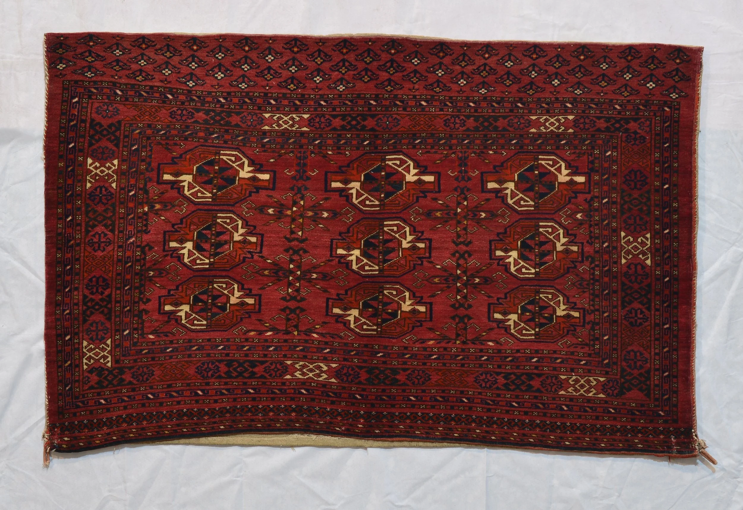 Turkmen cushion cover 11435, with rows of geometric guls on a red field and narrow patterned borders, 140 by 83 cm.