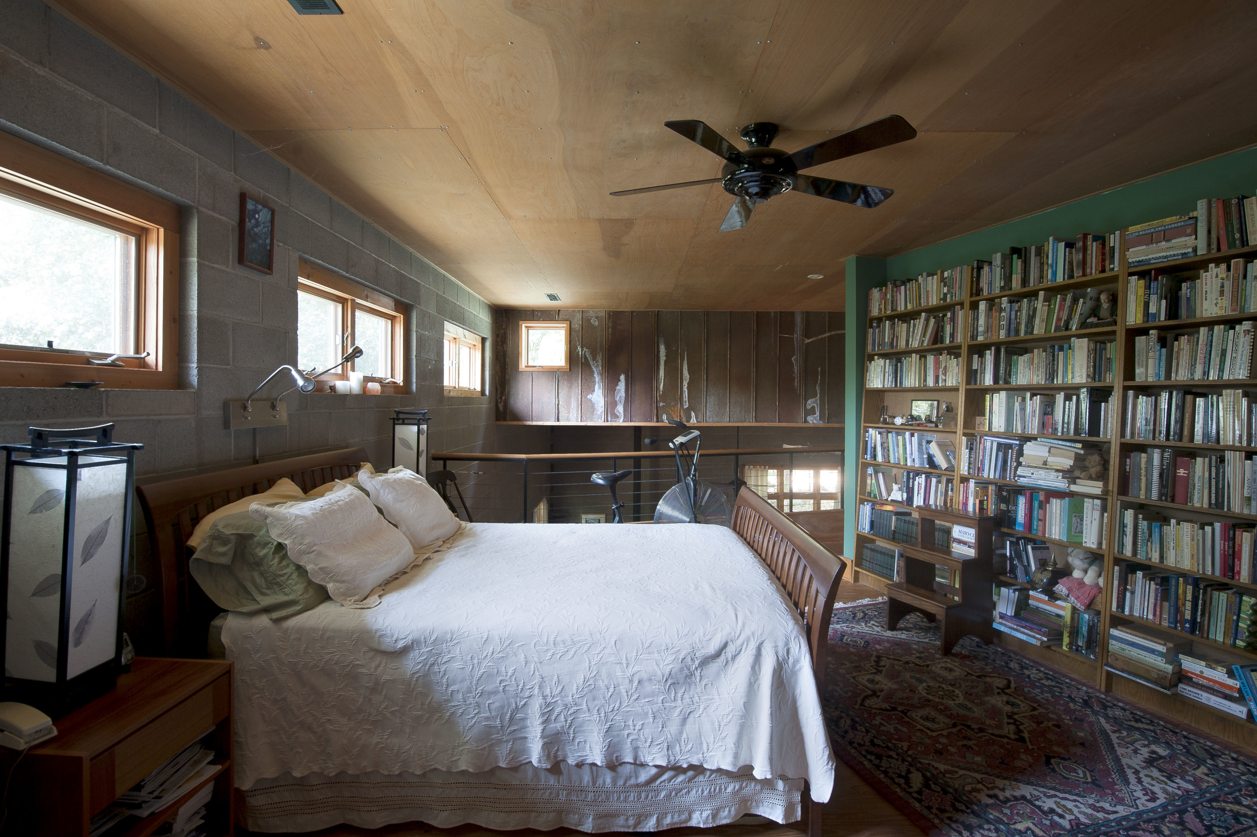 A long bookshelf wall and natural wood ceiling offer warmth to the master bedroom loft.