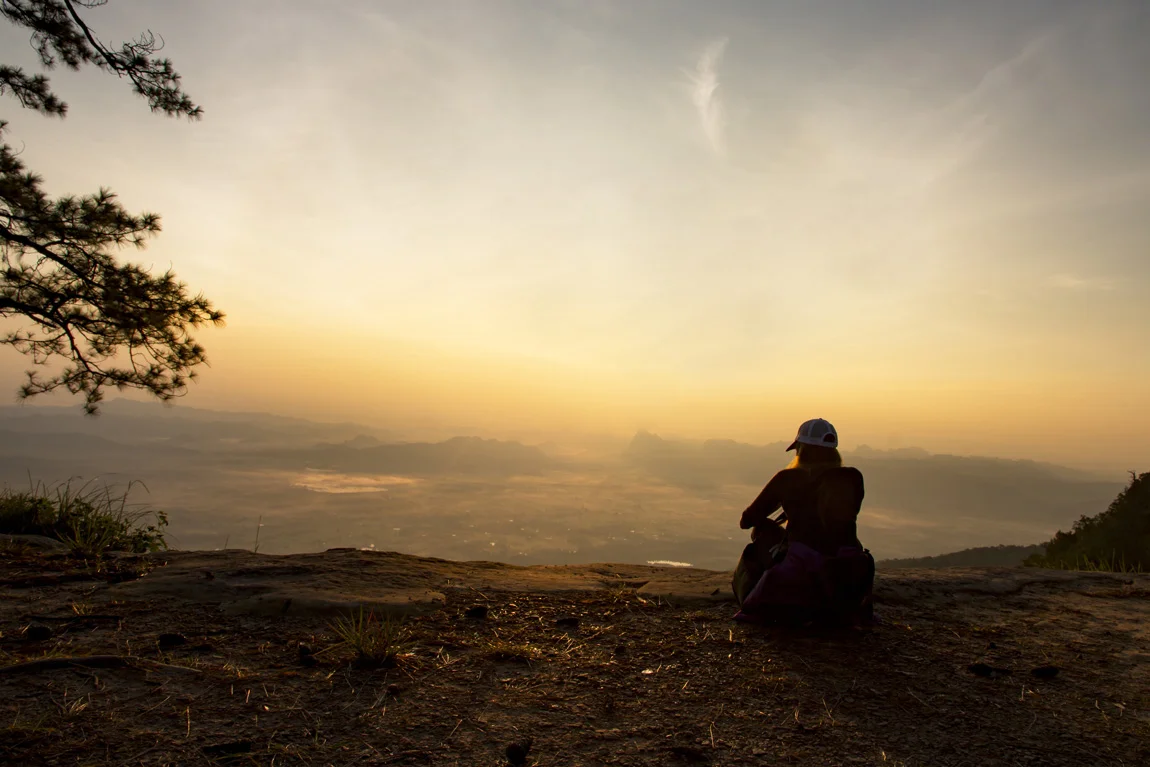 Person sitting on mountain looking out over valley and contemplating