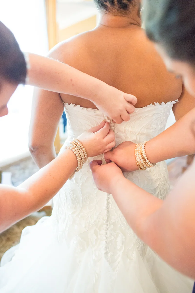 friends buttoning bride into her gown