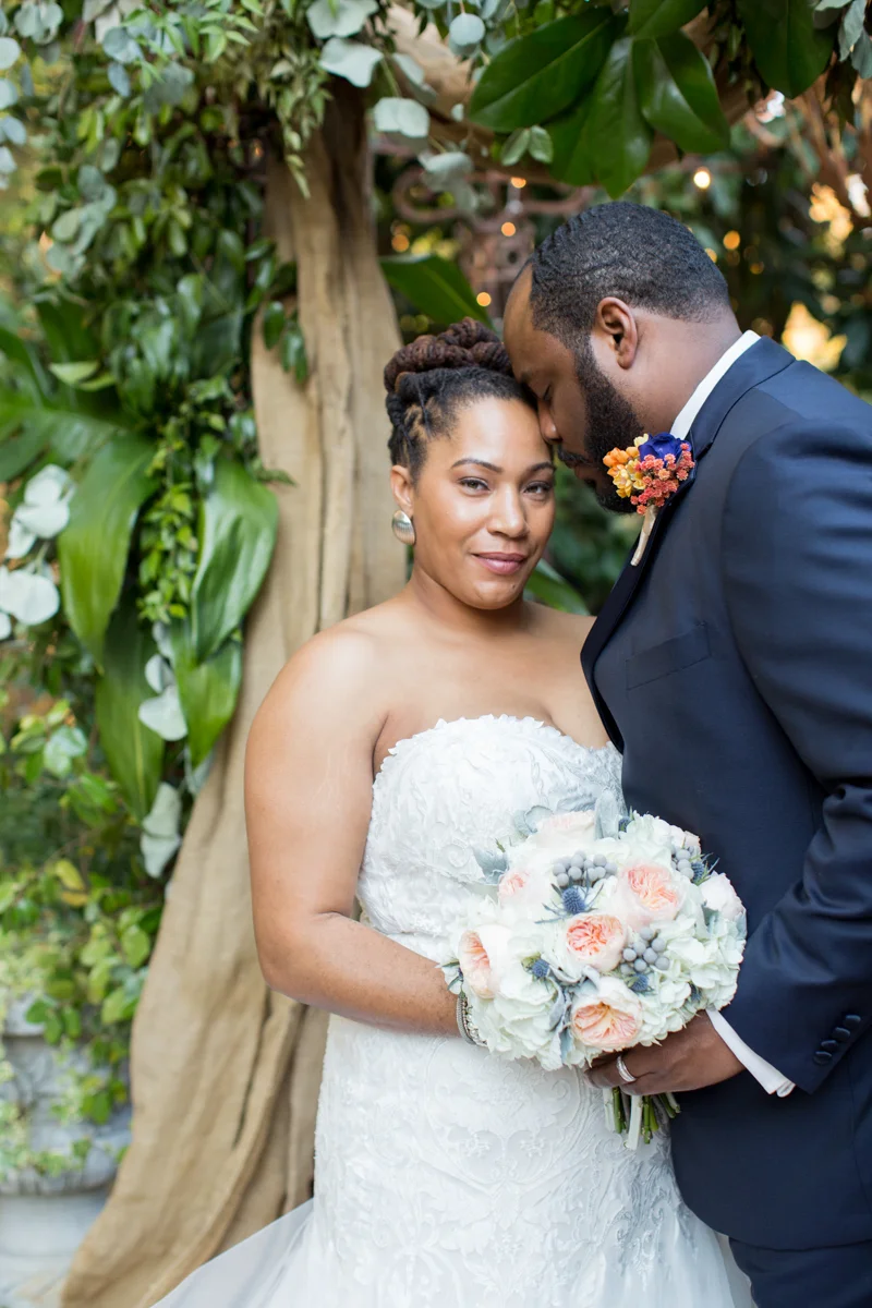 Black bride and groom posing at their wedding arch