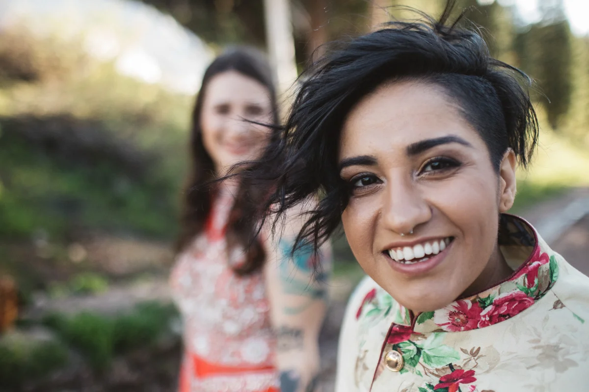 DENVER SAME-SEX INDIAN WEDDING MONICA SMILING AT CAMERA WITH ALBERTINE IN BACKGROUND