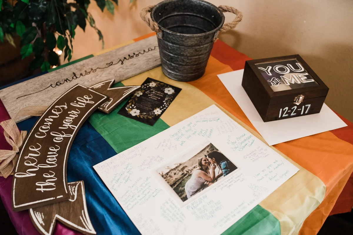 Rustic italian wedding table draped with LGBTQ+ flag; card box, picture, bucket, signs
