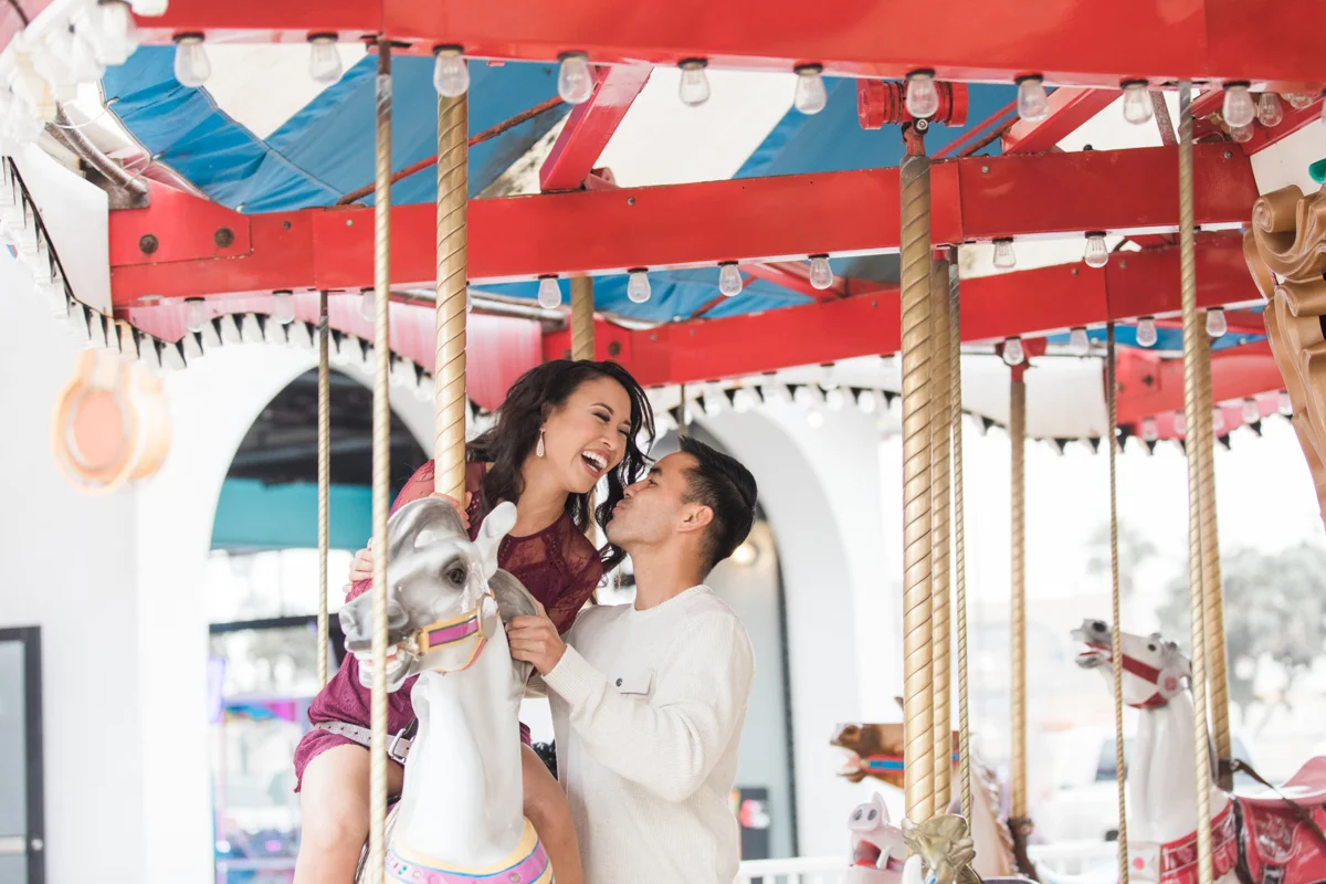 belmont park engagement session san diego angela laughing on carousel horse with jamie standing beside her