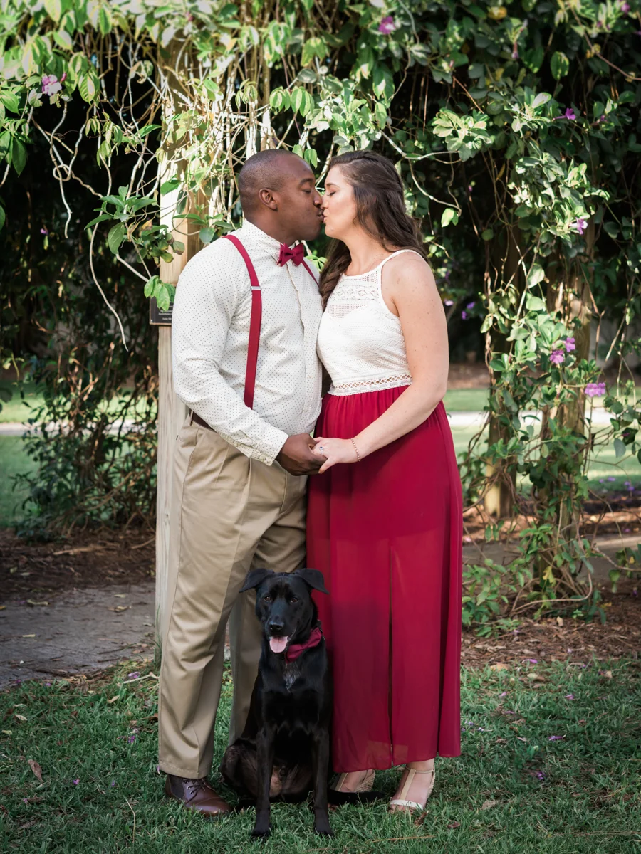 BOCA RATON ENGAGEMENT SESSION KISS UNDER TREES WITH DOG SITTING IN FRONT OF COUPLE