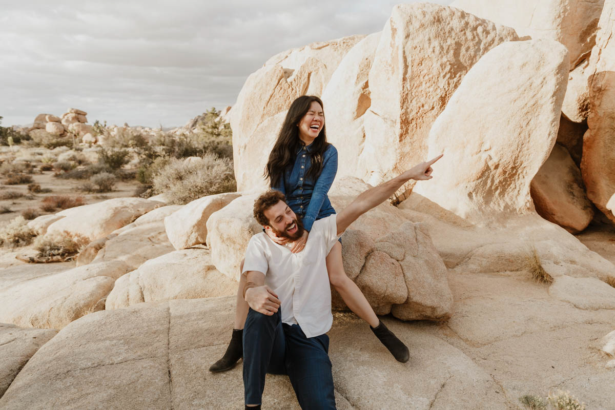 joshua tree california engagement session eda sitting above matt on rocks, matt pointing at something out of frame