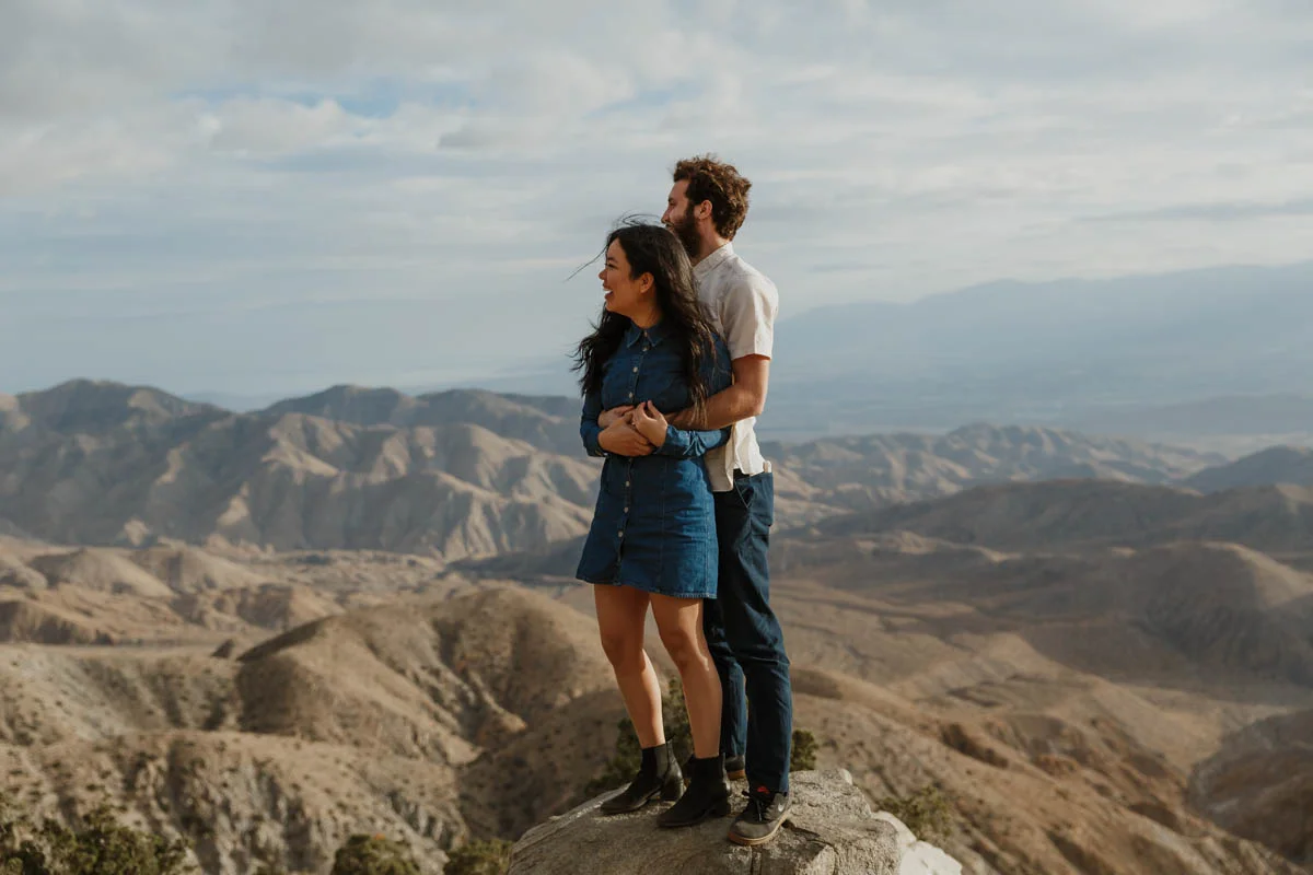 joshua tree california engagement session embrace on top of rock, mountains in background