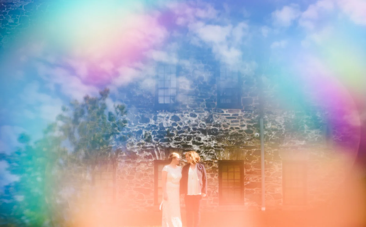 BALTIMORE WEDDING AT MOUNT WASHINGTON MILL DYE HOUSE COUPLE OUTSIDE STONE HOUSE, TRANSPARENT RAINBOW AND CLOUD OVERLAY