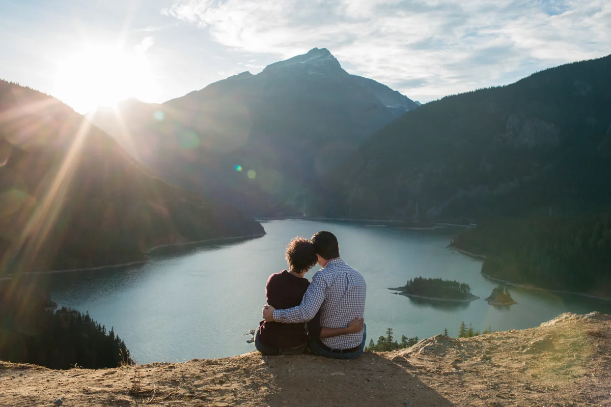 Diablo lake engagement session couple sitting on ledge looking at sun setting behind mountains