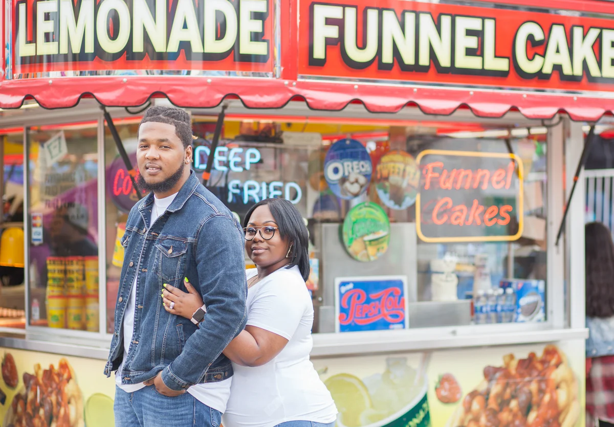 CARNIVAL PHOTO SHOOT DURHAM NORTH CAROLINA BRITTANY AND DEON IN FRONT OF CARNIVAL FOOD BOOTH