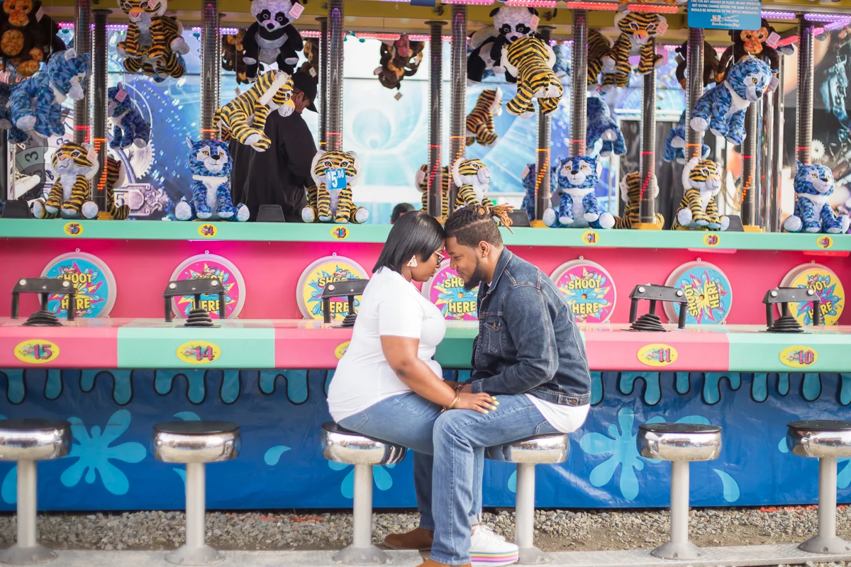 CARNIVAL PHOTO SESSION DURHAM NORTH CAROLINA BRITTANY AND DEON SITTING ON STOOLS IN FRONT OF GAME, THEIR FOREHEADS TOGETHER