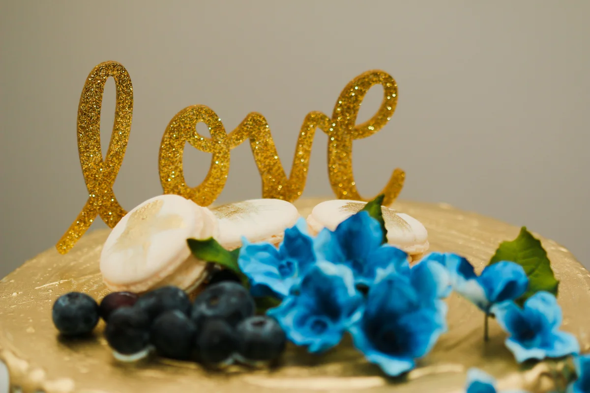 rialto theatre wedding cake with glitter "love" decal, blueberries, flowers, and macaroons topping