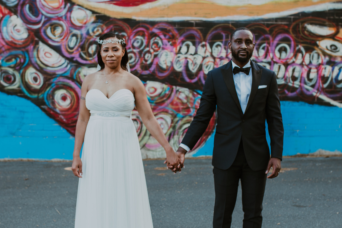 art-inspired levine museum wedding couple holding hands with mural in background