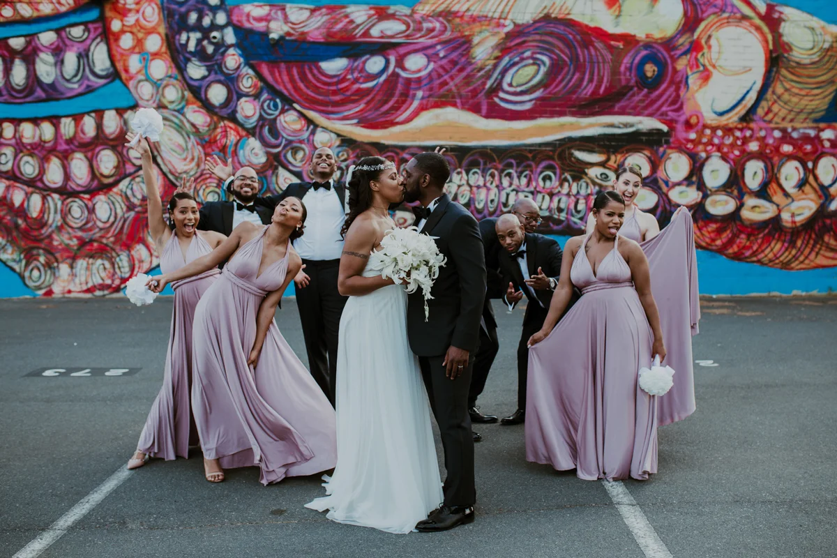 art-inspired levine museum wedding couple kissing with wedding party being silly behind them