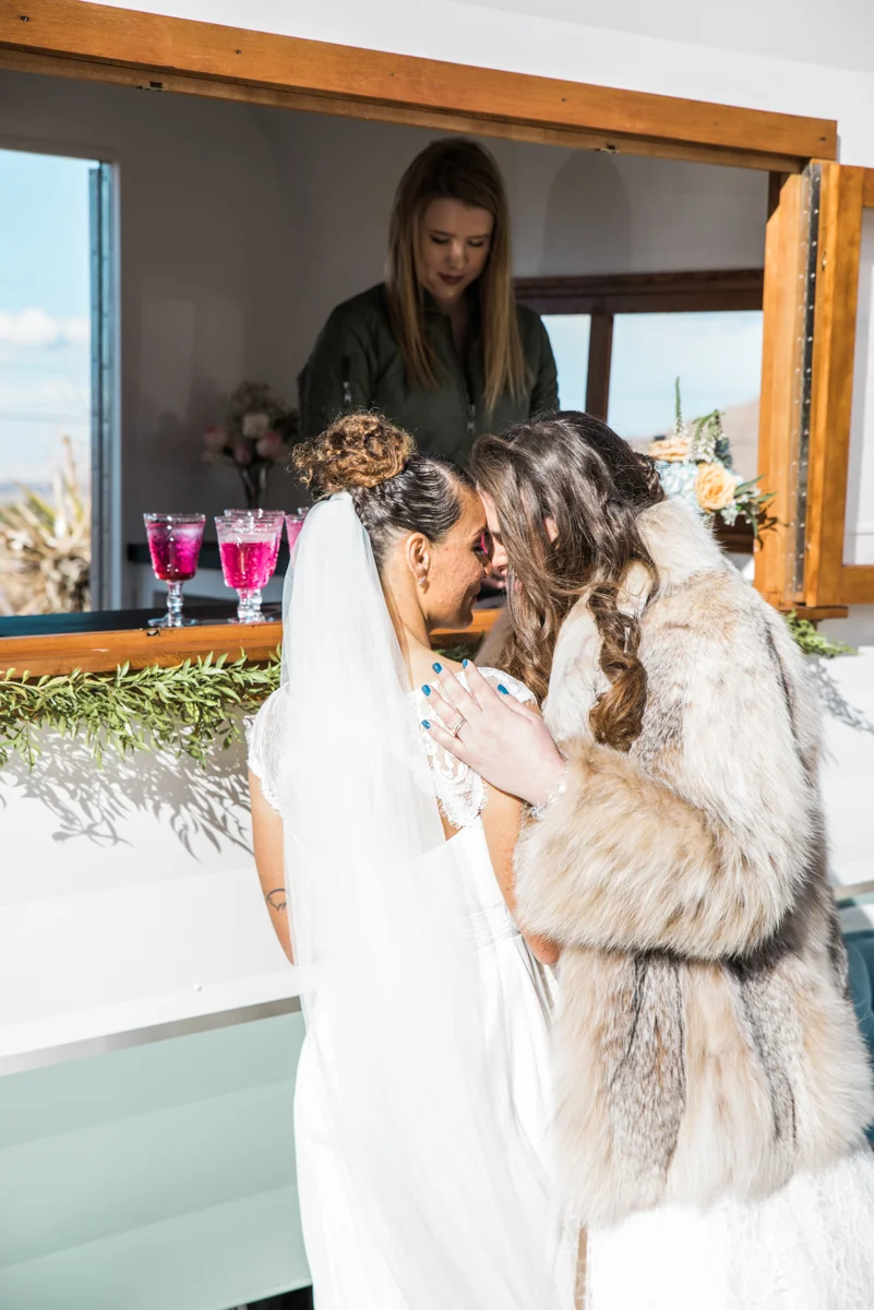 multi-cultural desert elopement brides embrace in front of bar