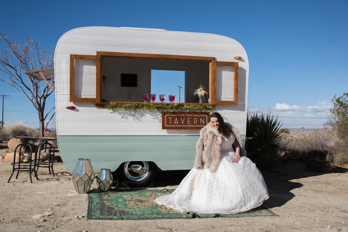 multi-cultural desert elopement bride sitting in front of trailer where drinks are served