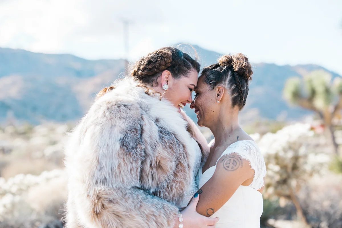 multi-cultural desert elopement brides embrace with mountains in background