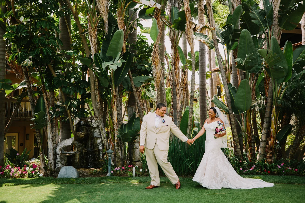 San Diego Tropical-Inspired Wedding william leading janelle by the hand in garden, palm trees in background