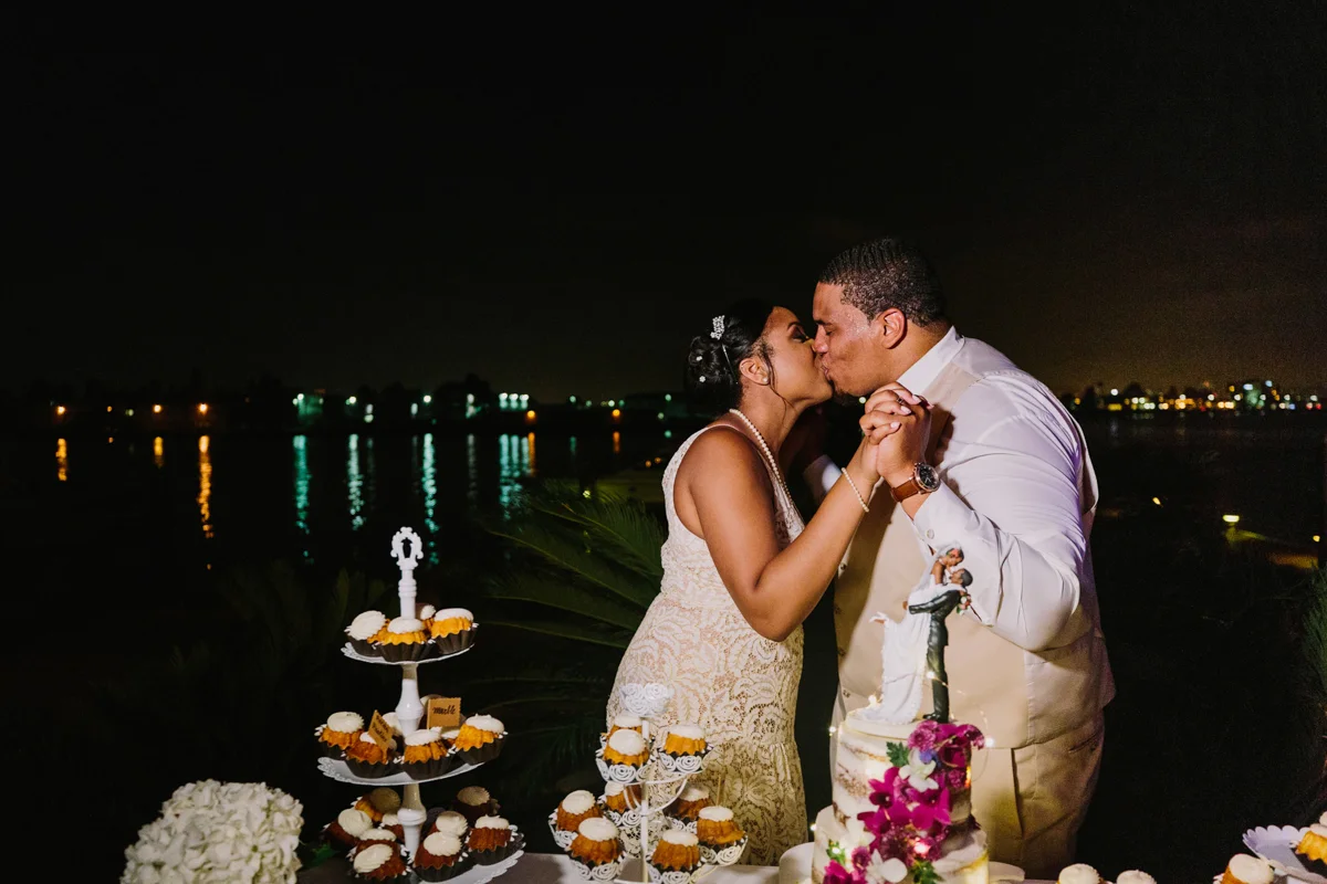 San Diego Tropical-Inspired Wedding couple kissing by dessert table with ocean and nighttime lights of city in background