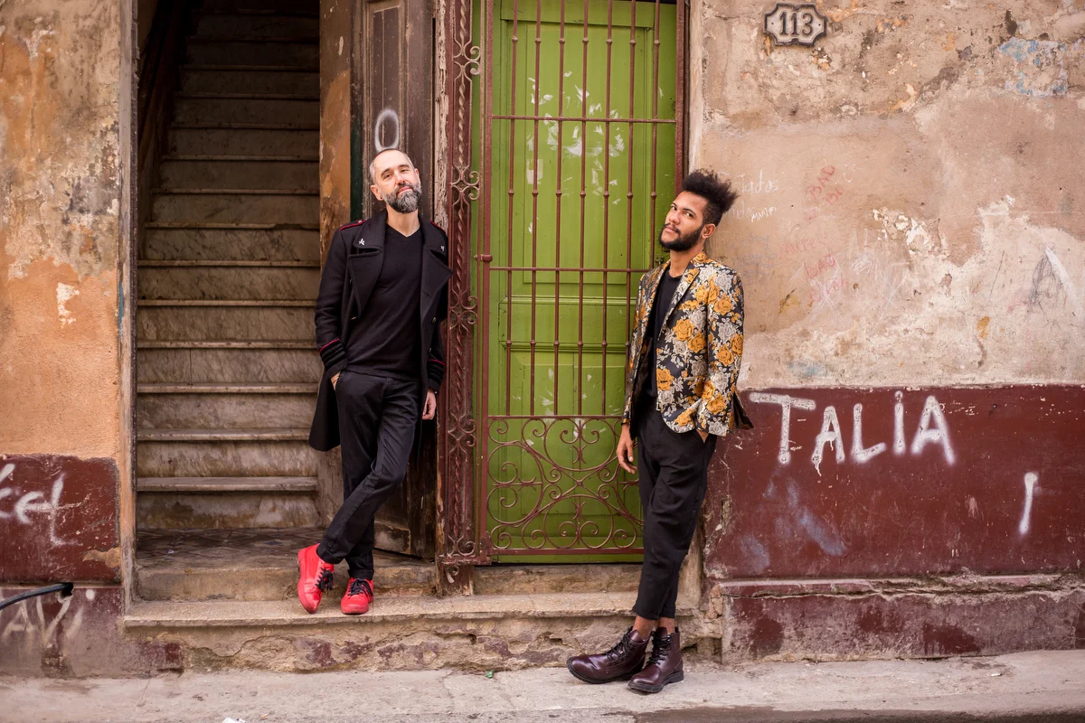 lovers in havana felix and ishak leaning on graffitied wall, staircase leading up into a building behind them
