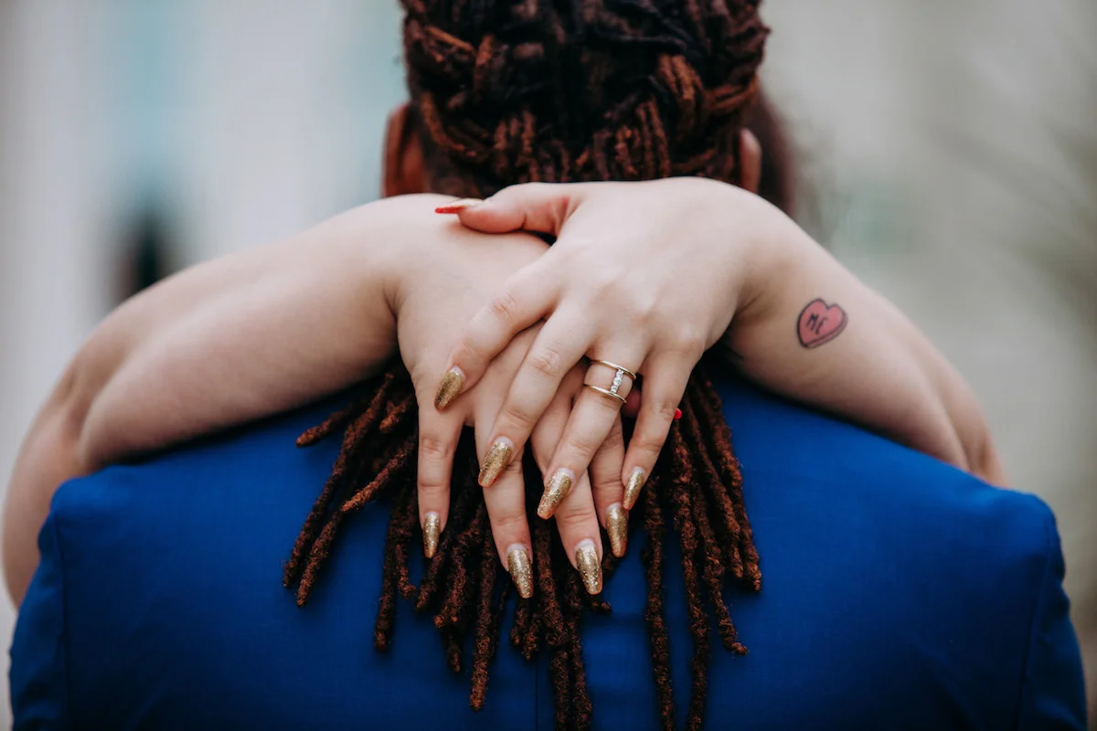 engagement photo shoot at akron art museum alysse’s arms around gio, focusing on engagement ring