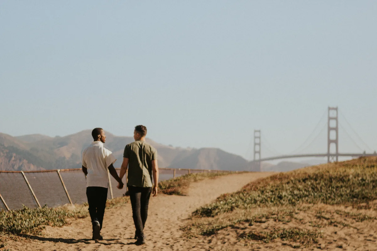 couples session baker beach san francisco california caleb and eugene walking hand in hand down sandy path with view of golden gate bridge