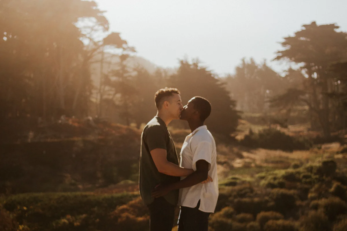 couples session baker beach san francisco california kiss with trees and hilly landscape in background