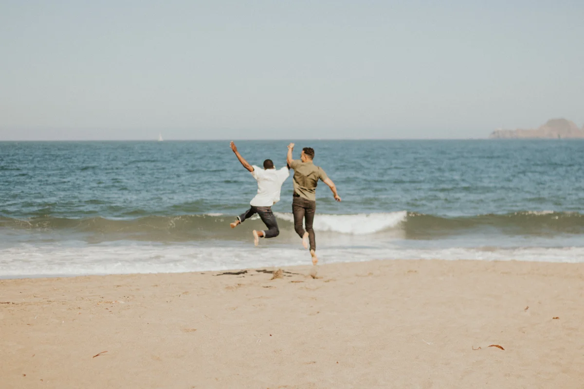 couples session baker beach san francisco california caleb and eugene leaping as they run toward the ocean holding hands