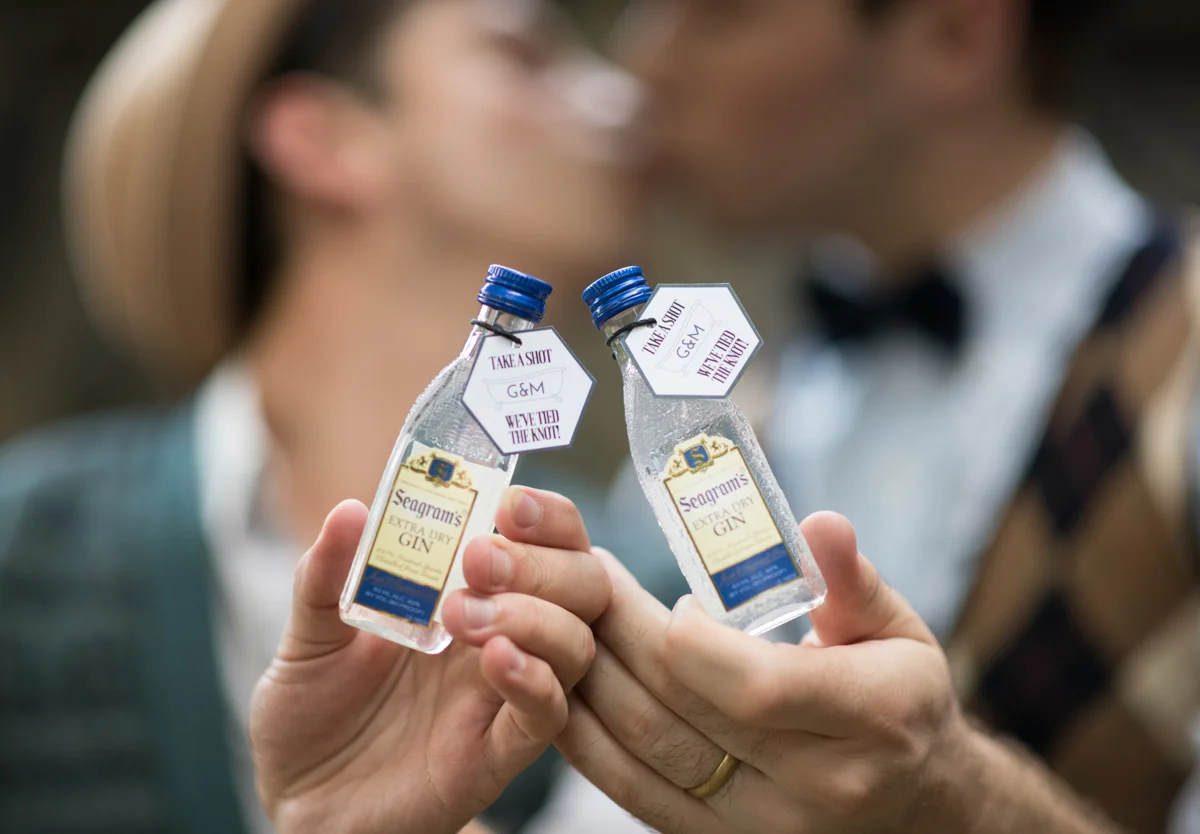 vintage wedding editorial at the art factory paterson new jersey kiss while holding mini bottles of gin for guest favors; tags read “take a shot, we’ve tied the knot!”