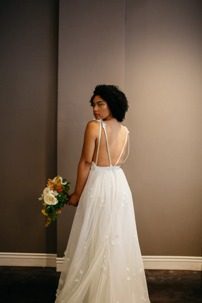 wes anderson inspired wedding styled shoot columbia south carolina bride looking over shoulder holding bouquet, back of gown featured
