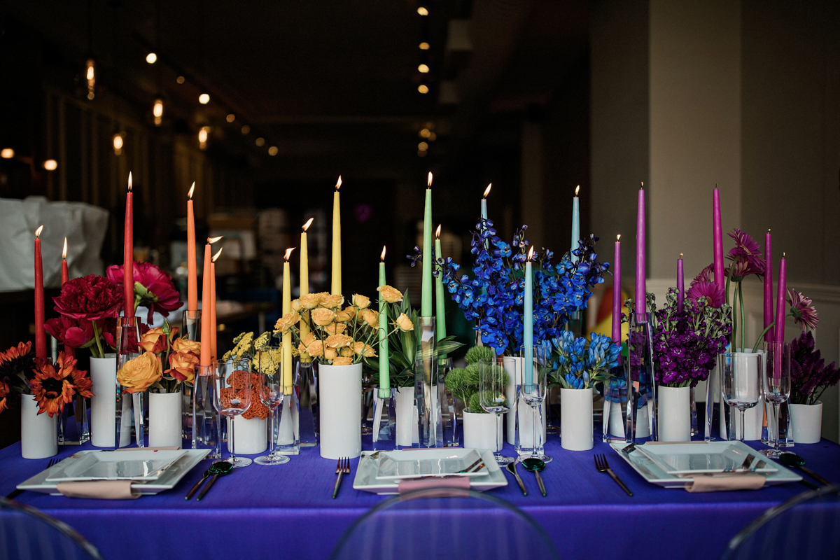 80s themed pride party brooklyn new york set table with rainbow spectrum of taper candles and vases of flowers