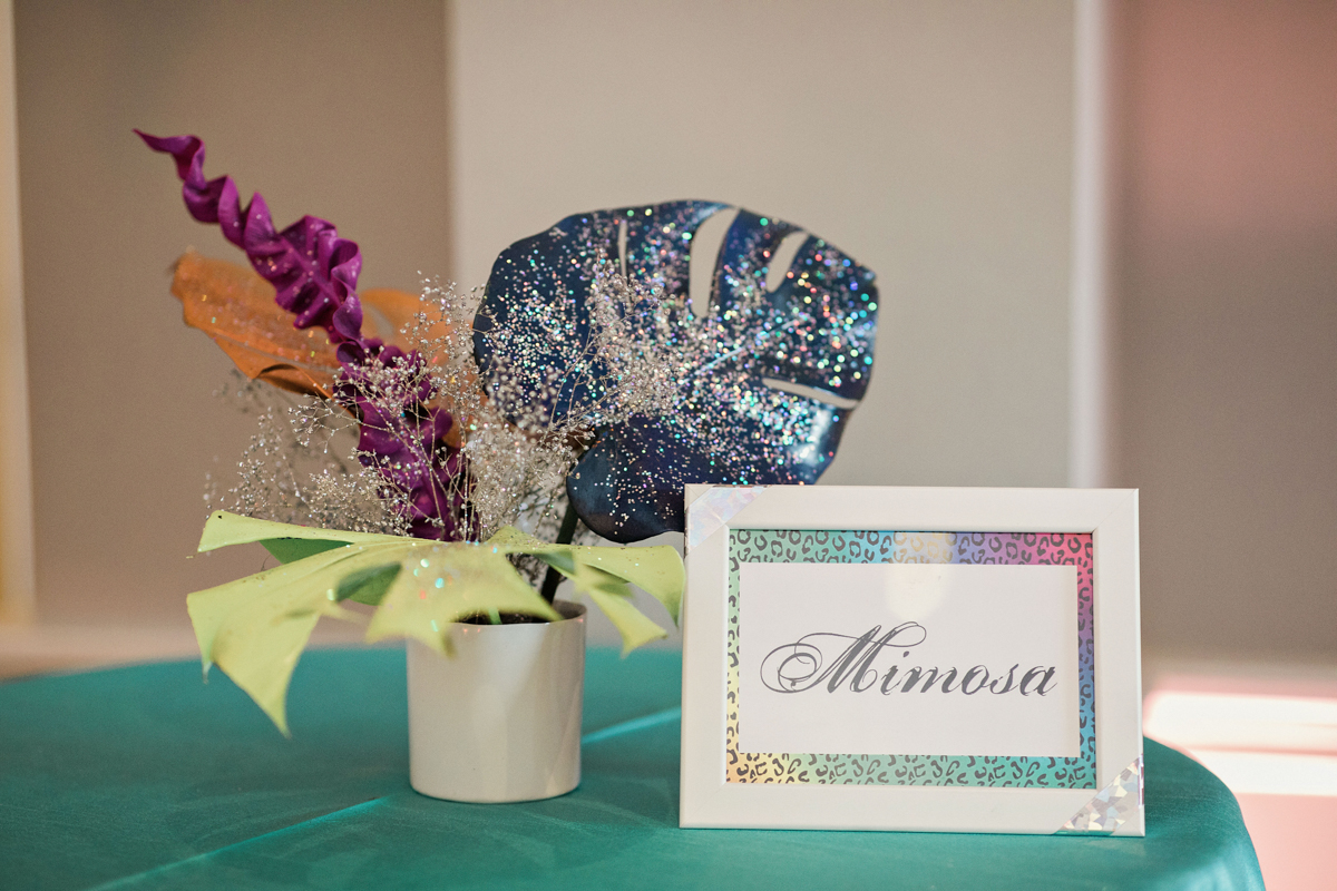 80s themed pride party brooklyn new york glittery florals in small vase, card on table reading “mimosa”
