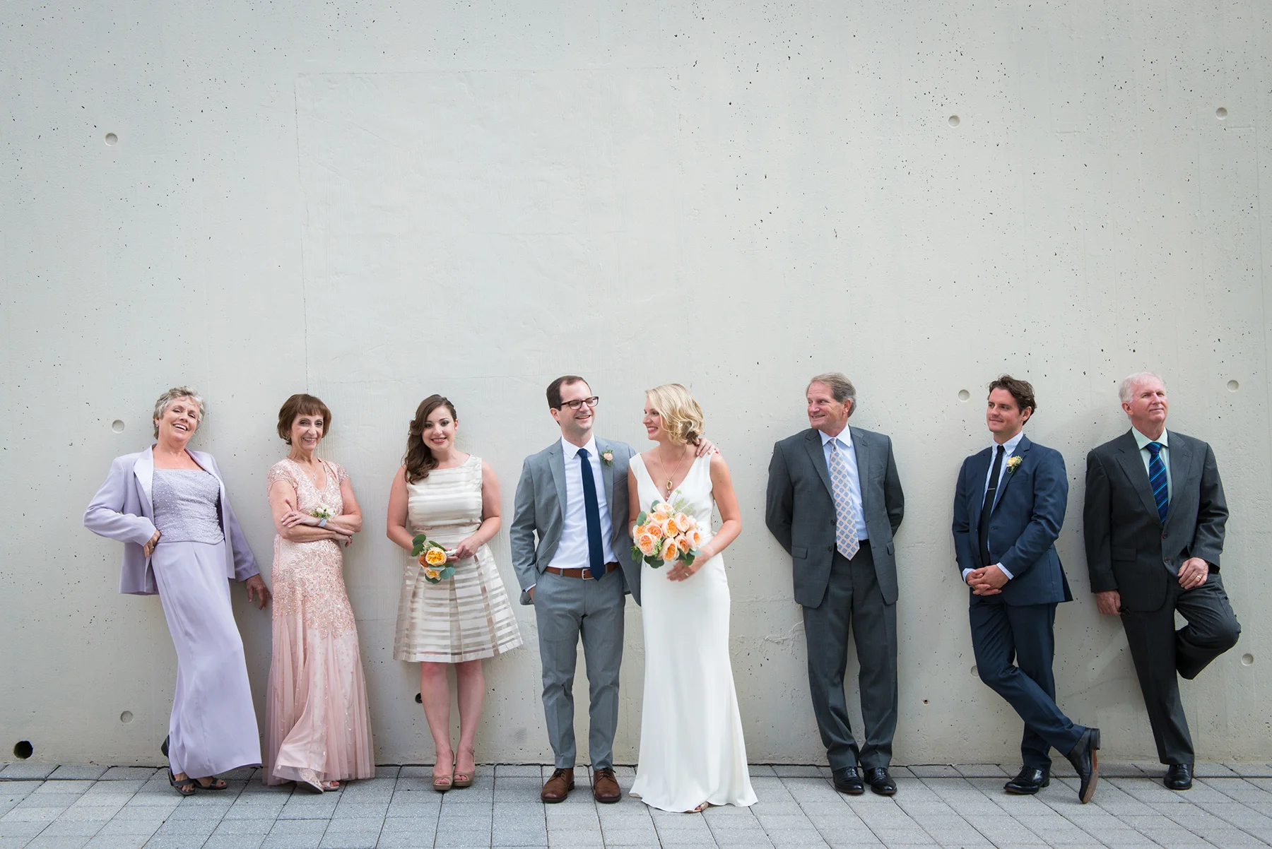 couple posing with wedding party in front of gray wall michelle schapiro photography