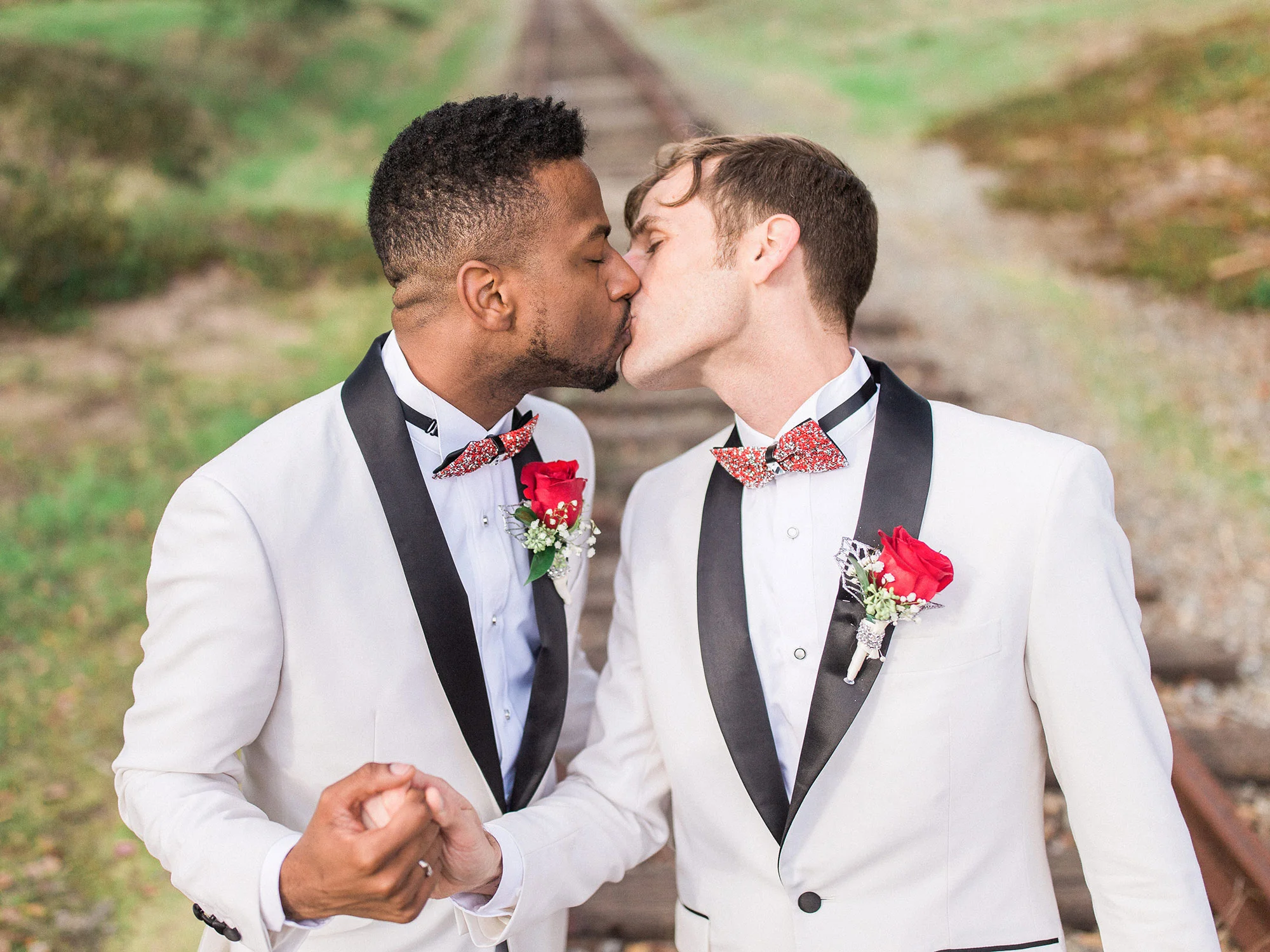 two grooms in matching suits kissing and holding hands in a field after their wedding Apollo Fotografie San Francisco
