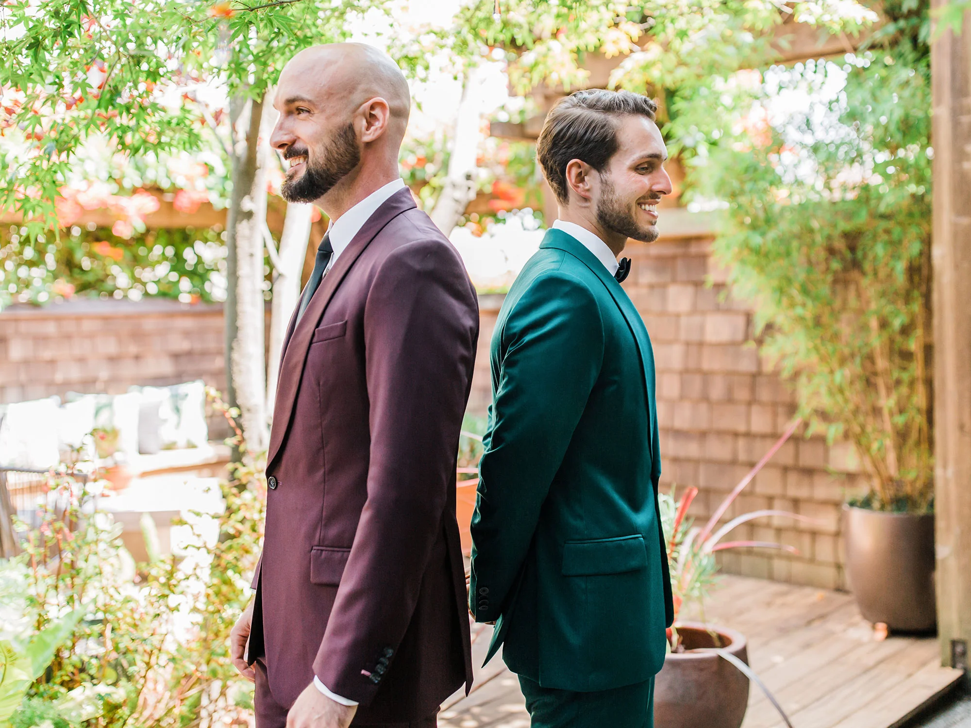 two grooms in velour suits standing back to back in garden at wedding Apollo Fotografie San Francisco