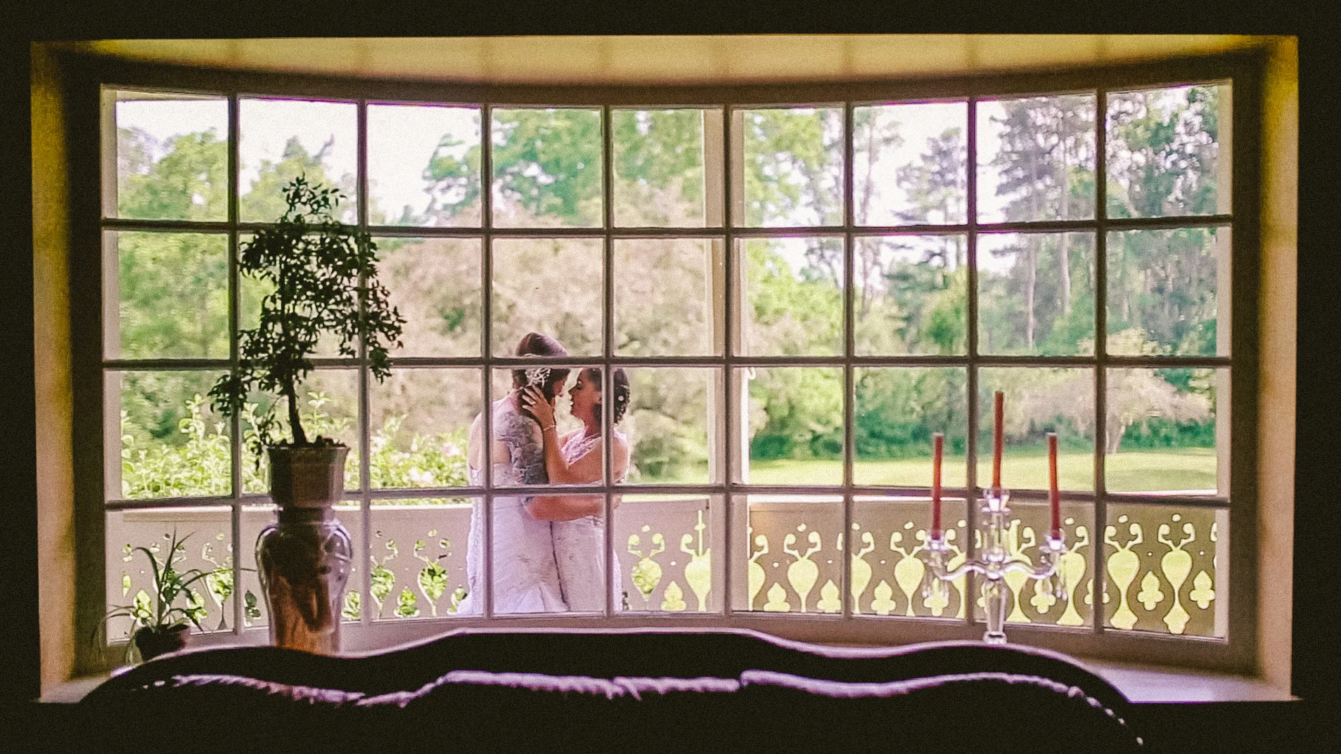 Portrait through a window of two brides leaning in for a kiss Philadelphia PA Love More Films