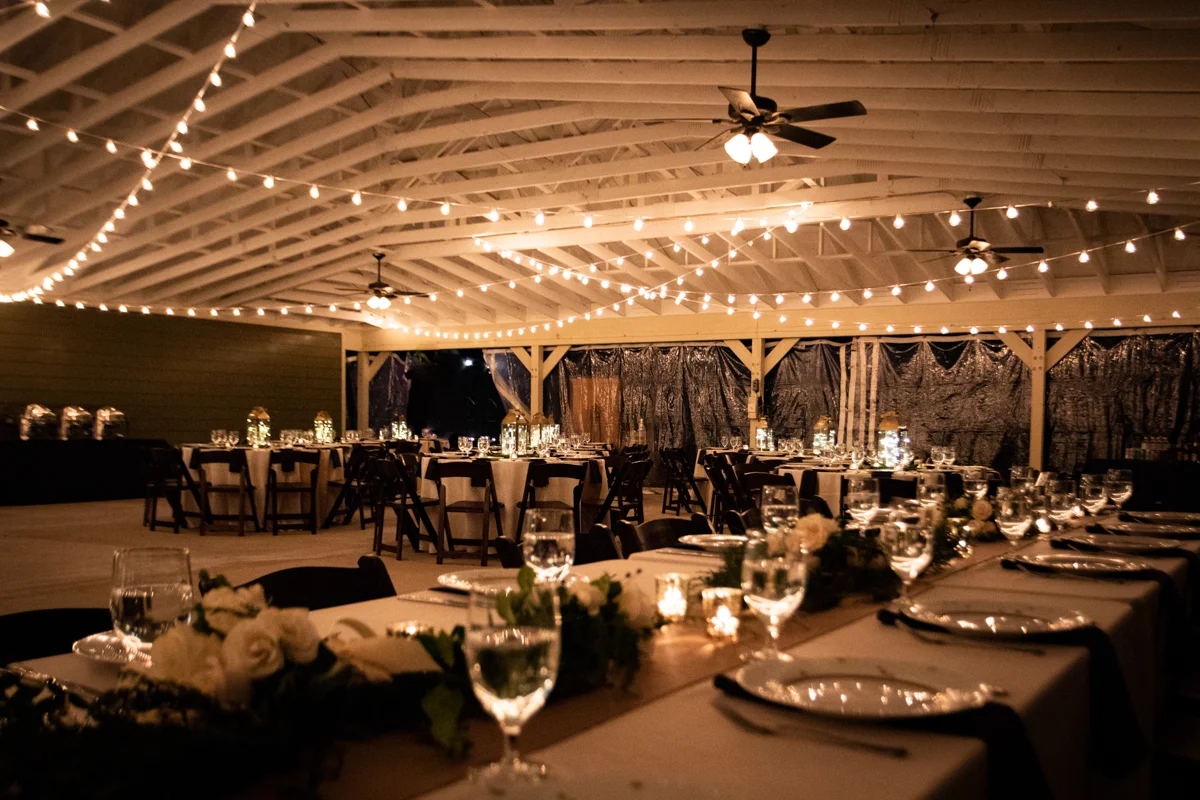 Romantic, Intimate-Feeling Wedding reception venue with tables and white lights hanging from high rafters