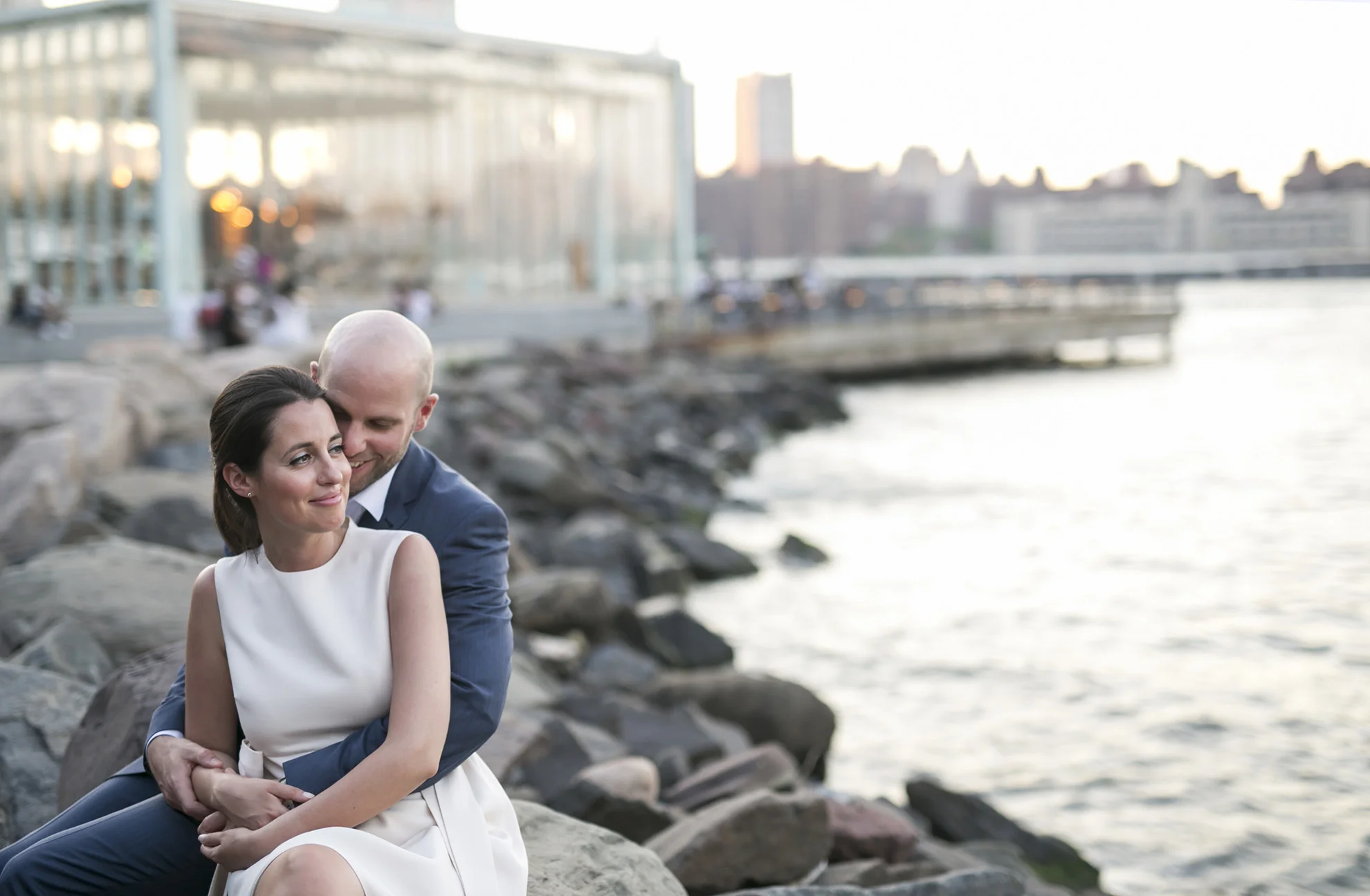 bride and groom sitting on rocks by east river in an embrace after their wedding