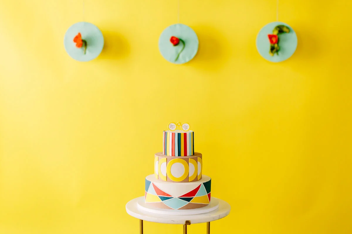 wes anderson inspired wedding brooklyn new york cake against yellow wall with three floral art pieces