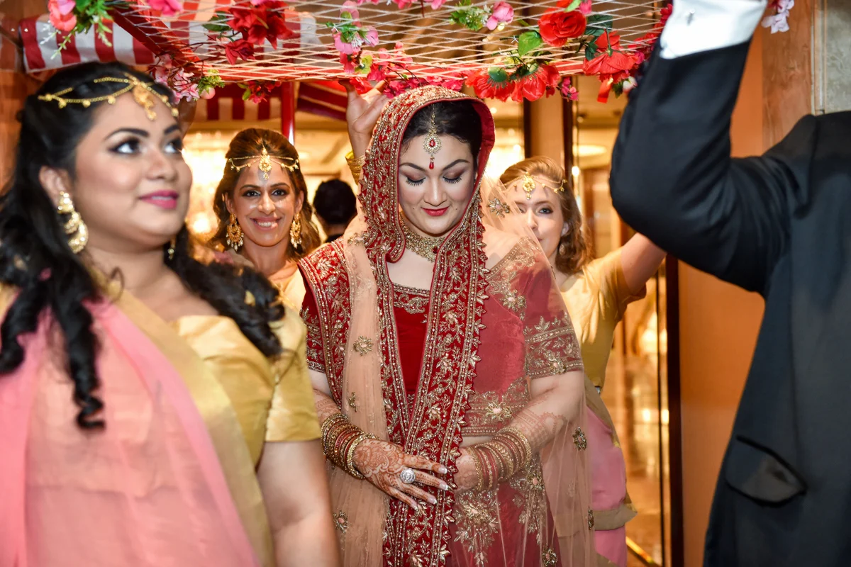 Mita walking down the aisle into the Indian wedding ceremony under a DIY bed of flowers