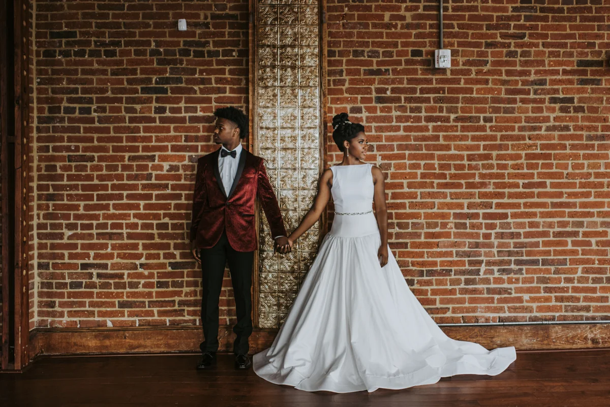vintage vegan glam in Washington DC HFB Photography couple holding hands in front of brick wall, looking away from each other