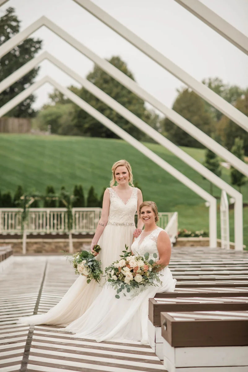 PAVILION WEDING KANSAS CITY MISSOURI Hey Tay Photography brides posing together, hannah standing and meredith sitting on bench