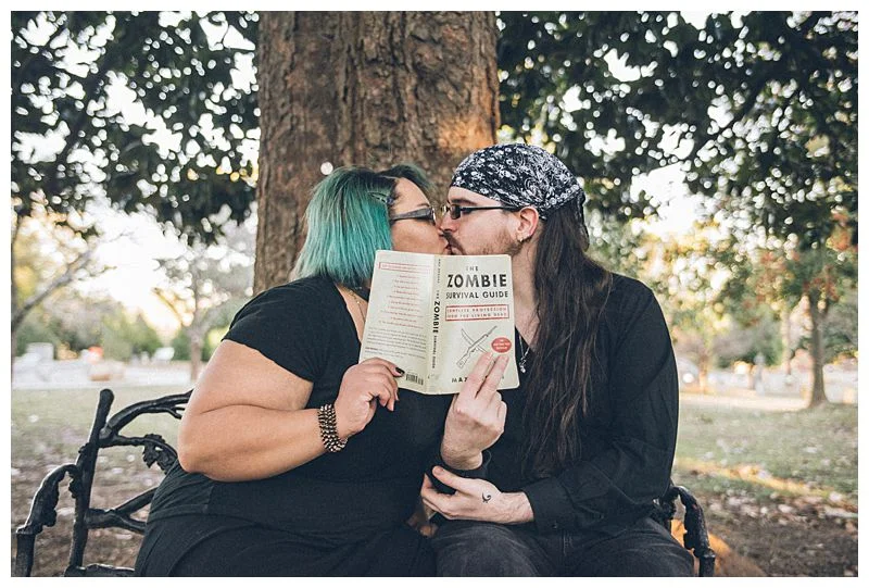 Engaged couple kisses behind Zombie Survival Guide book Sharma Shari Florida Wedding Photographer