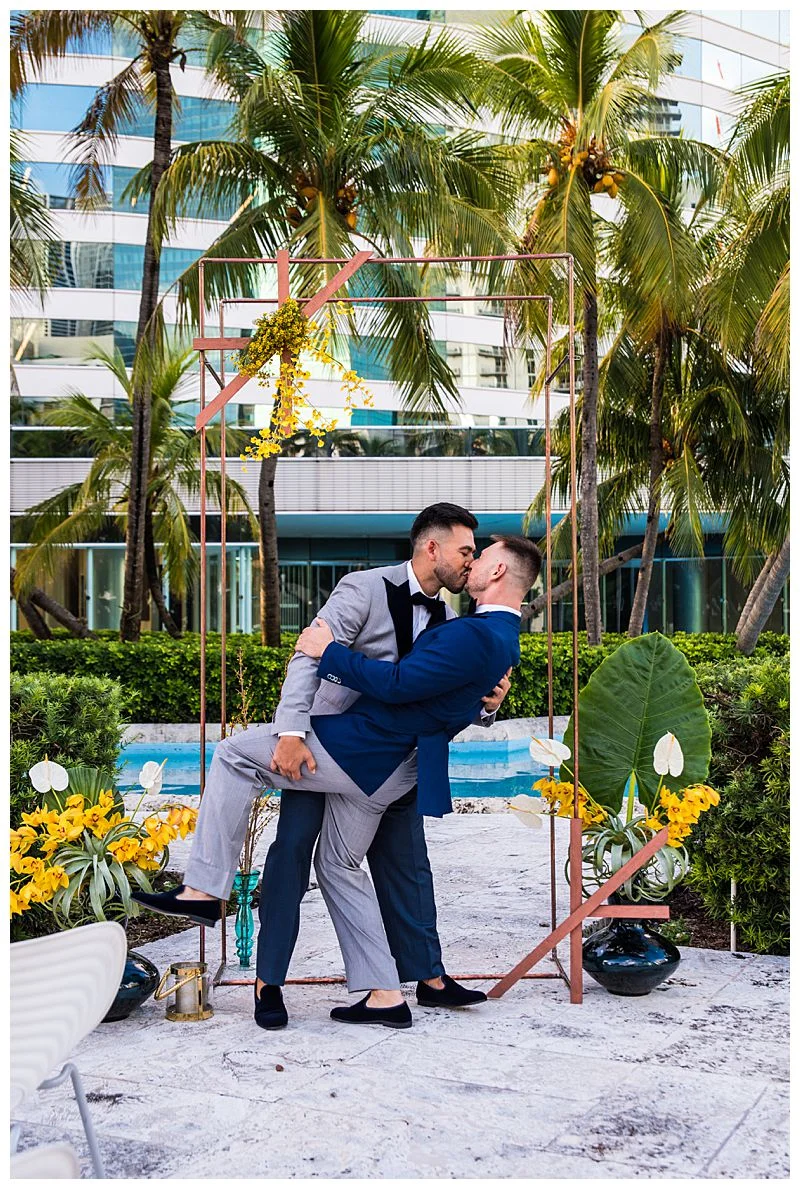 two grooms share a kiss under palm trees for tropical wedding Sharma Shari Florida Wedding Photographer