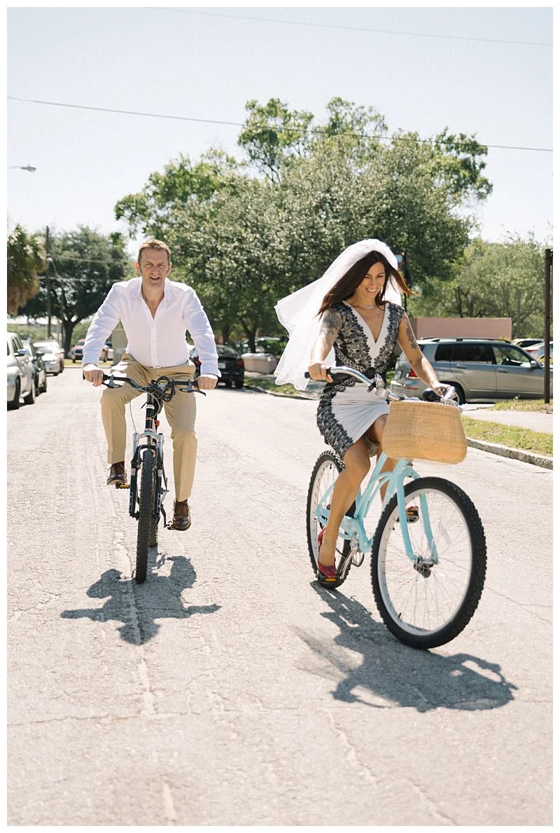 groom and bride with veil ride bikes after their wedding Sharma Shari Florida Wedding Photographer