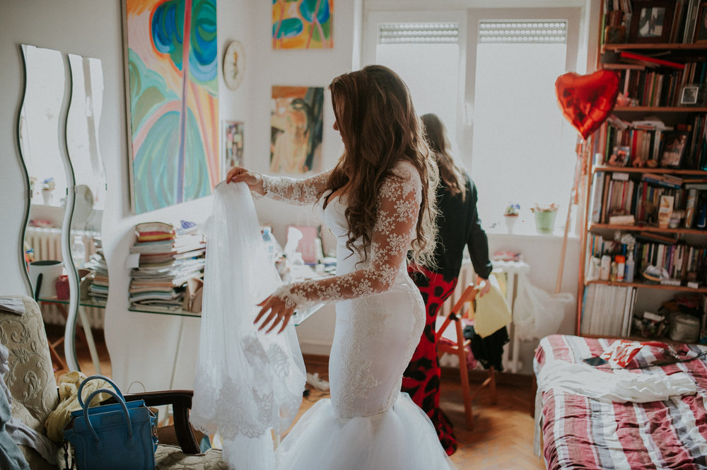 Sofia getting ready in DIY wedding dress surrounded by parents’ paintings serbia Aleska and Mina Photography